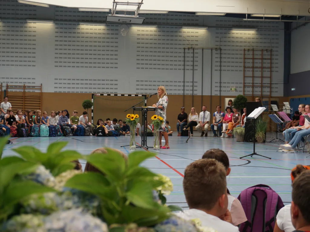 Person spricht am Mikrofon, im Vordergrund ein Blumenstrauß.